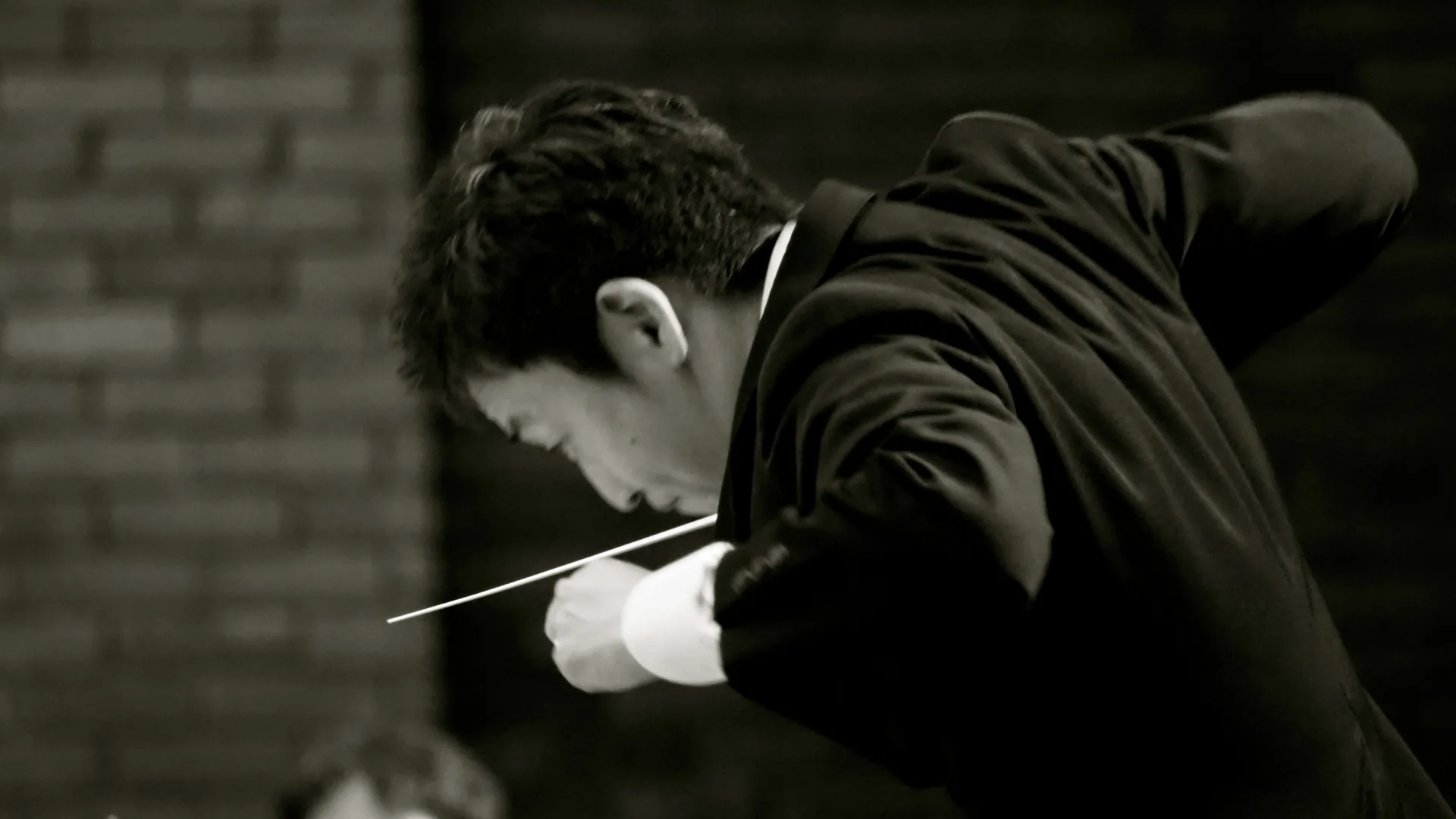 Black and white close-up of a conductor’s hands in motion, expertly guiding an orchestra with a baton, symbolizing strategic leadership and the art of orchestration in program management.